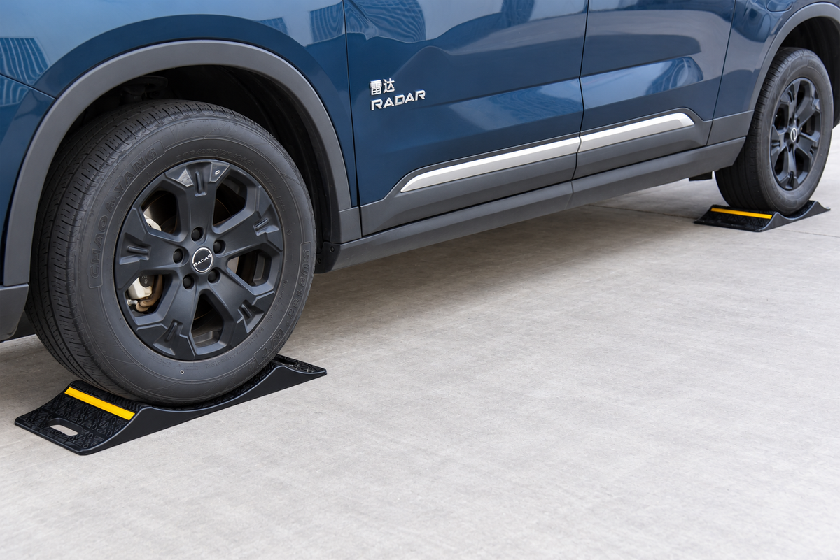 Vehicle front and rear wheels positioned on heavy-duty double-sided parking mats