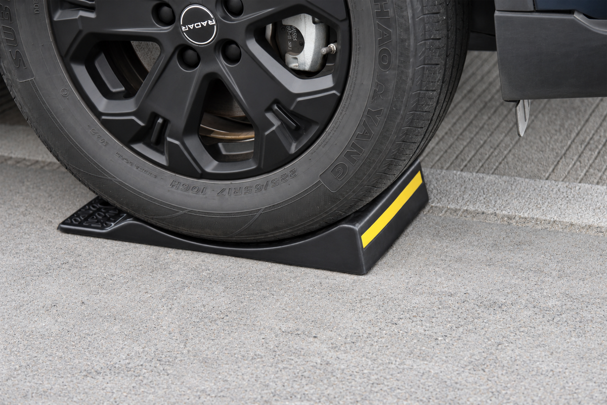 Side view of a vehicle tire positioned against the raised stop of a heavy-duty single-sided parking mat