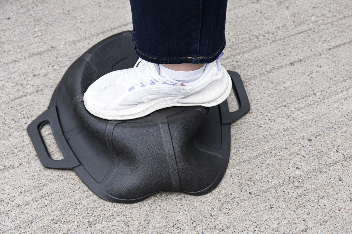 Inverted black rubber feed pan showing base deformation under a shoe