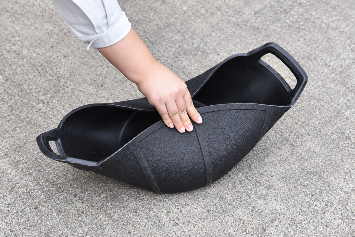 Hand pressing the sides of a black rubber feed pan inward to demonstrate flexibility