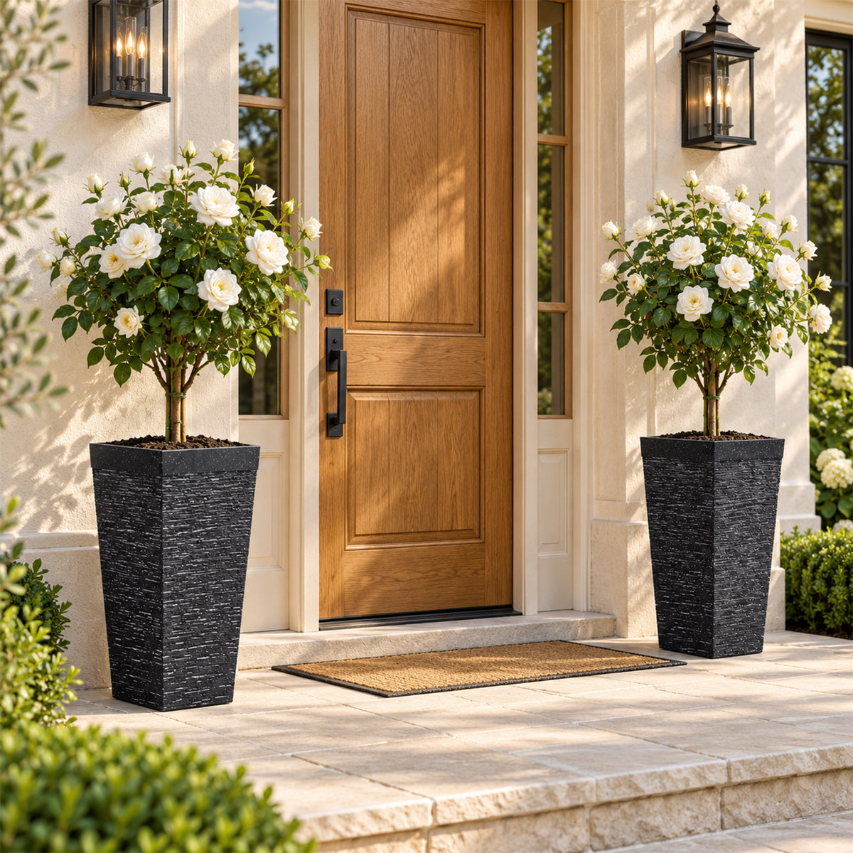 Two black tall square planters with flowering plants beside a front door