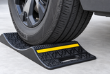 Angled close-up of a vehicle tire on a heavy-duty parking mat showing yellow reflector and carry handle