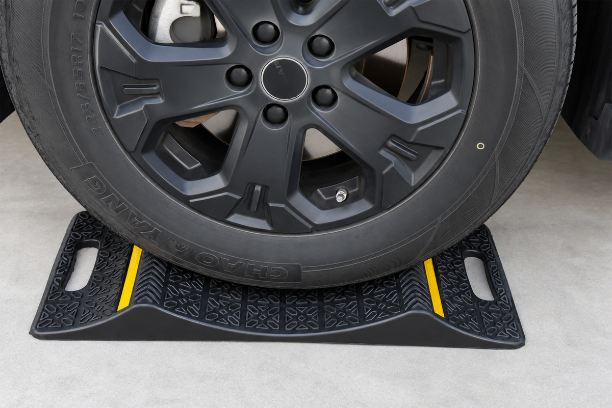 Vehicle tire resting between the raised ridges of a double-sided parking mat with yellow reflective strips