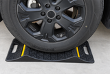 Vehicle tire resting between the raised ridges of a double-sided parking mat with yellow reflective strips